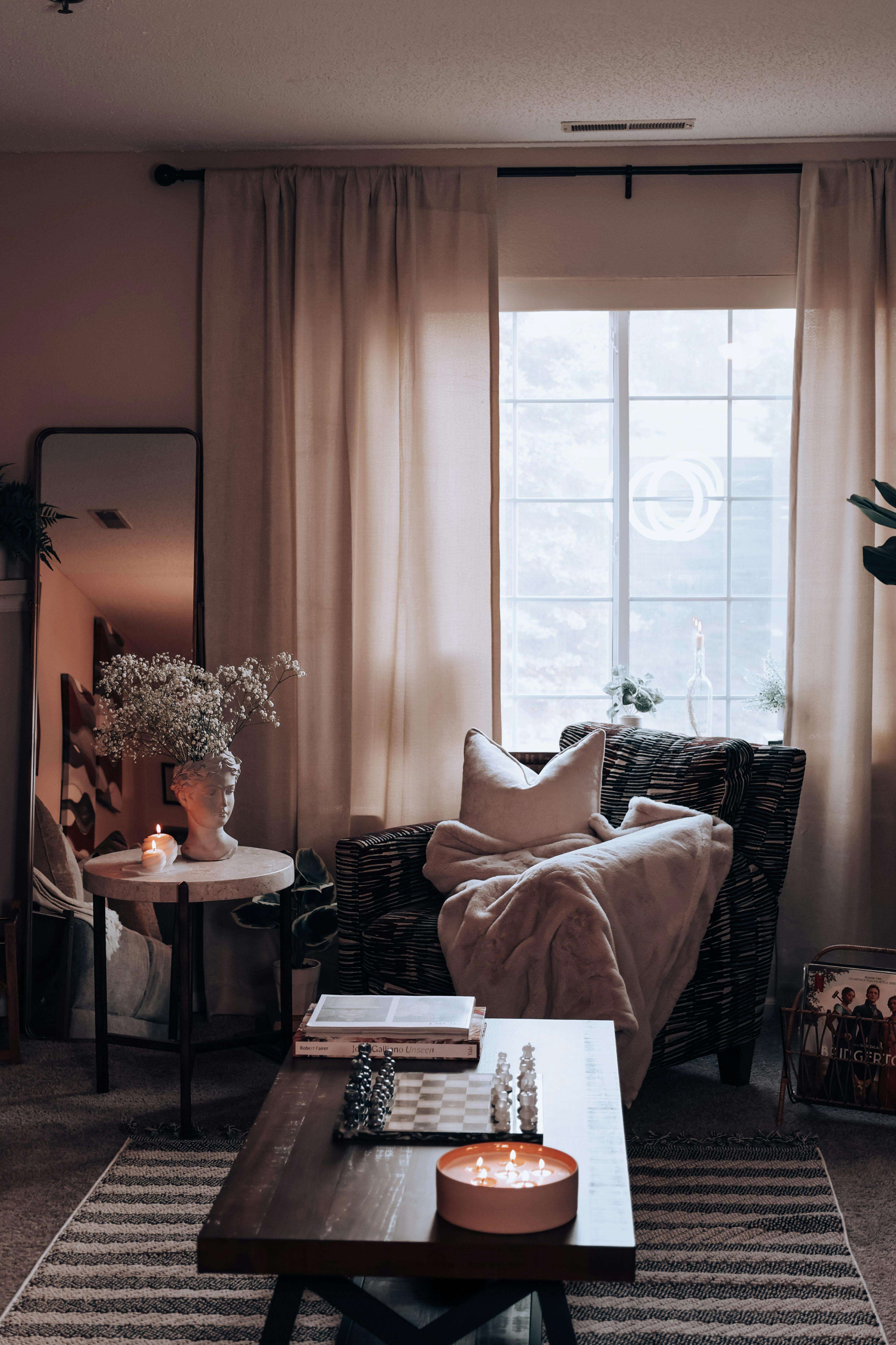 Cozy living room with a chessboard on a dark wooden coffee table, a warm candle, and a striped armchair with a soft blanket nearby.